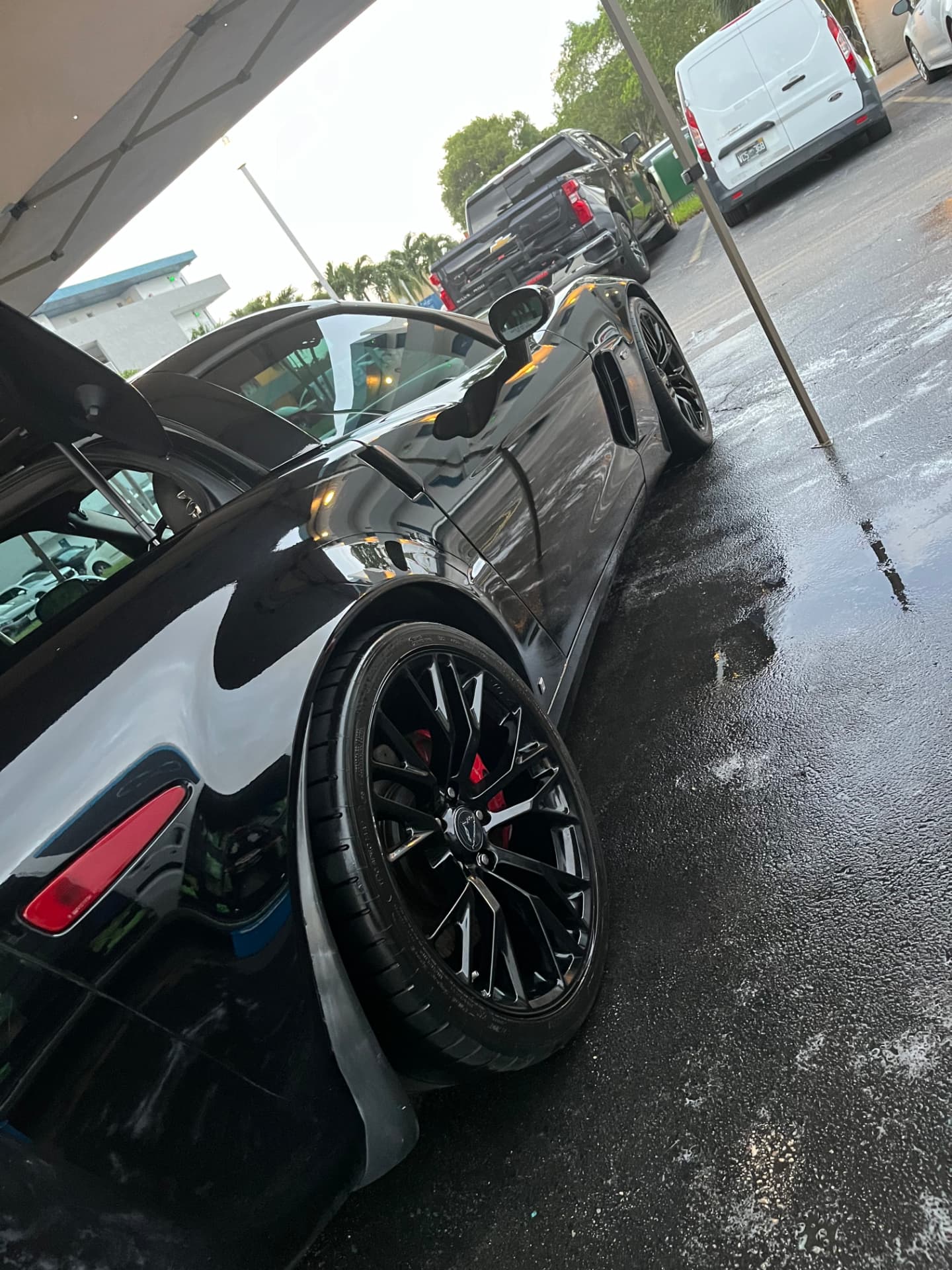 Gloss black sports car under the wash canopy, ground still wet